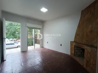 A sala apresenta um piso de madeira e uma parede de pedra no interior da residência.