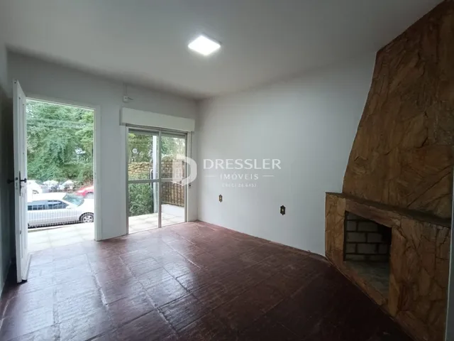 A sala apresenta um piso de madeira e uma parede de pedra no interior da residência.