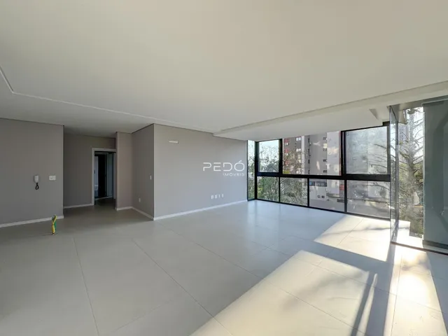 Sala de estar ampla com piso claro e grandes janelas de vidro.