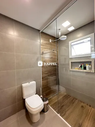 Banheiro com revestimento de azulejos claros e box de vidro transparente.