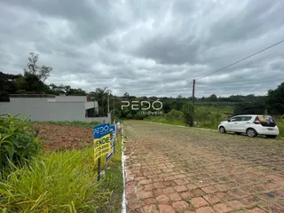 Vista externa de uma propriedade com um pátio de tijolos e vegetação ao fundo.