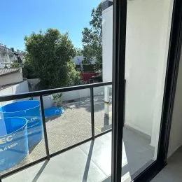 Uma vista externa da varanda com grade de vidro e vegetação ao fundo.