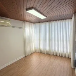 Sala de estar com piso de madeira e cortinas brancas cobrindo a janela.