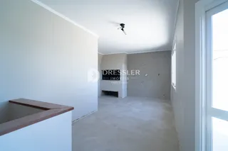 A foto mostra um corredor interno com paredes brancas e piso de concreto.