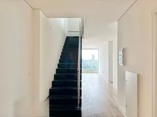 Hall de entrada com escadaria escura e vista urbana.