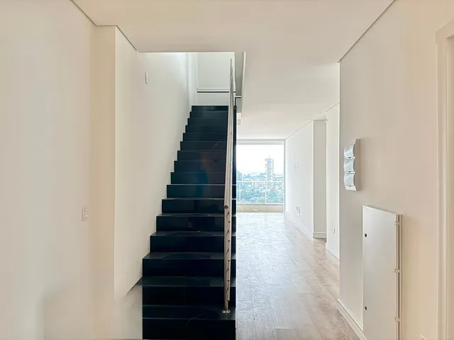 Hall de entrada com escadaria escura e vista urbana.