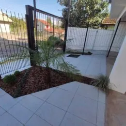Área externa pavimentada com piso de cerâmica e paisagismo.