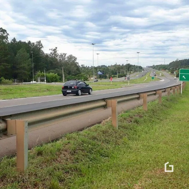 Vista de uma estrada com vegetação ao longo de uma cerca de proteção.