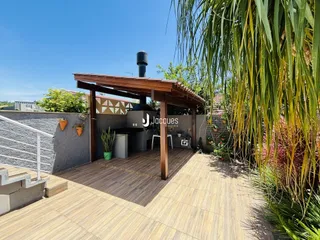 Vista externa de um pátio com deck de madeira e vegetação exuberante.