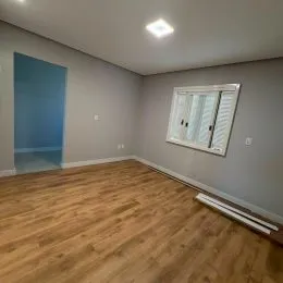 Interior de uma sala com piso de madeira clara e paredes neutras.