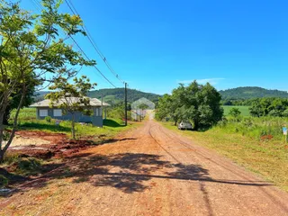 Vista da propriedade rural em Lajeado, Brasil, com estrada de terra e vegetação ao redor.
