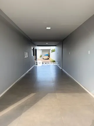 Corredor longo e iluminado com piso claro e paredes cinzas.
