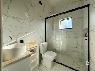 Banheiro com revestimento de mármore nas paredes e box de vidro.