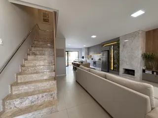 Vista de uma sala de estar com escadaria e cozinha moderna.