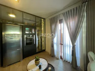 Sala de estar com grandes janelas e cortinas claras em um imóvel no Brasil.