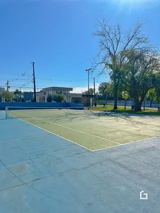 Uma quadra esportiva externa pavimentada com grama e árvores.