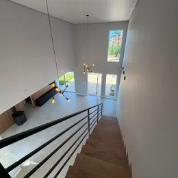 Vista de um corredor com piso de madeira e guarda-corpo escuro.