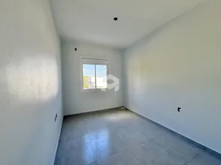 Uma sala de estar ampla com paredes brancas e piso de cerâmica clara.
