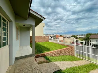 Vista externa da casa com muro de tijolos e cerca branca no quintal.