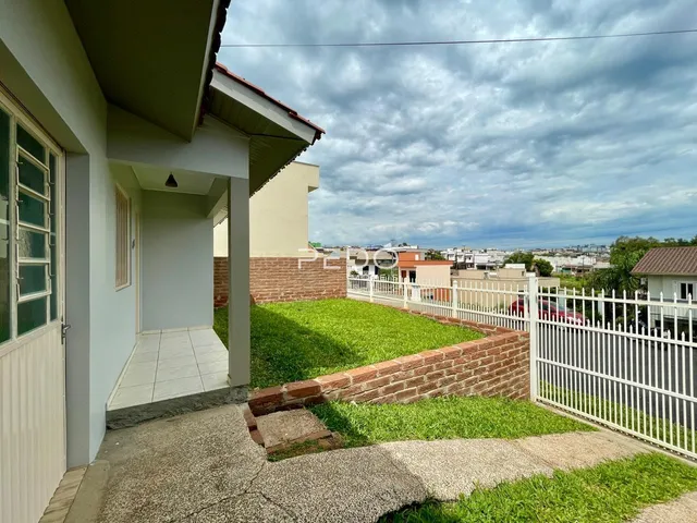 Vista externa da casa com muro de tijolos e cerca branca no quintal.
