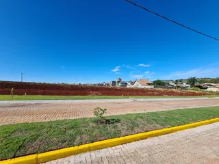 Vista externa de uma rua pavimentada com grama e campo aberto ao fundo.