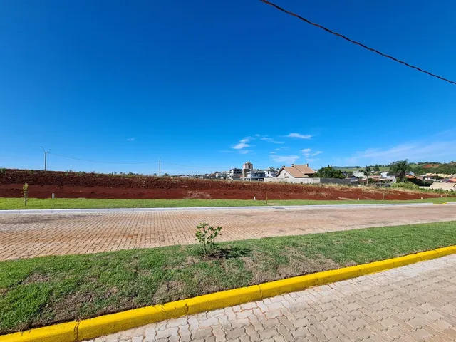 Vista externa de uma rua pavimentada com grama e campo aberto ao fundo.