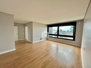 Ambiente interno amplo com piso de madeira clara e grande janela.