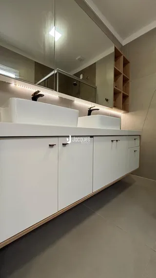 Foto de um banheiro com bancada branca e espelho no interior de uma residência.