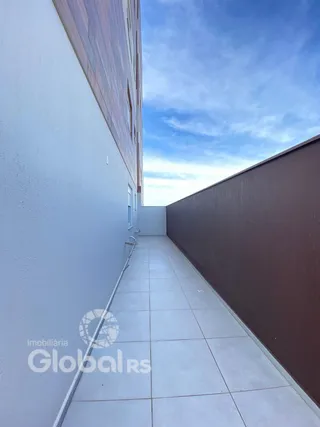 Vista de um corredor externo com piso de cerâmica entre paredes brancas e marrons.