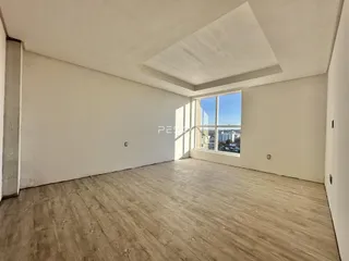 Ambiente interno de uma sala com piso de madeira e grande janela.