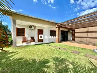Vista externa de uma casa residencial com jardim gramado e área coberta.