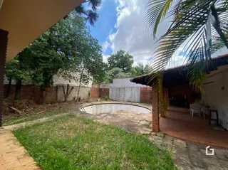 Vista externa de um jardim com muro de tijolos e área coberta.