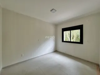 Imagem de uma sala de estar vazia com paredes brancas e piso claro.