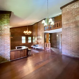 Ambiente interno de uma sala ampla com piso de madeira e paredes de tijolo aparente.
