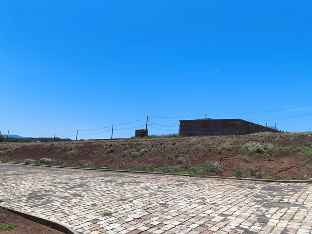 Paisagem de campo com terreno inclinado e estruturas ao fundo.