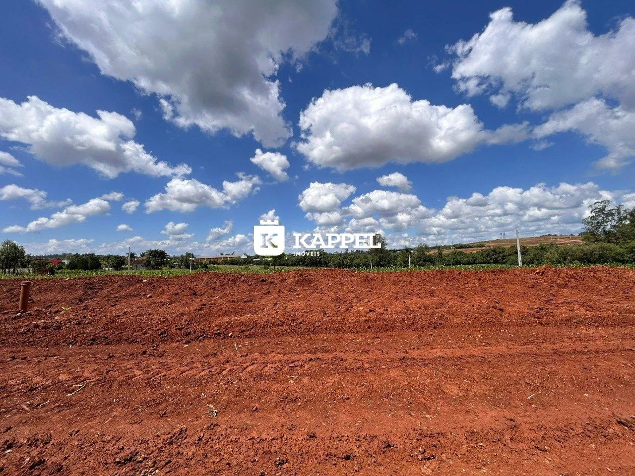 Campo de terra avermelhada sob um céu azul com nuvens.