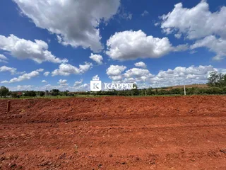 Campo de terra avermelhada sob um céu azul com nuvens.