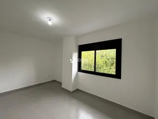 Uma sala de estar com paredes brancas e uma grande janela de madeira escura.