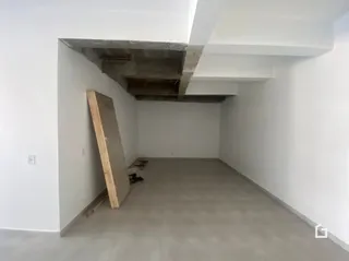 Interior de um espaço com teto de concreto aparente e parede branca.