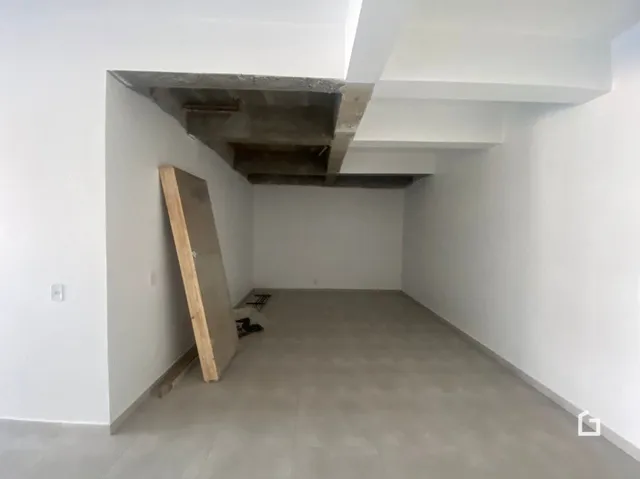 Interior de um espaço com teto de concreto aparente e parede branca.