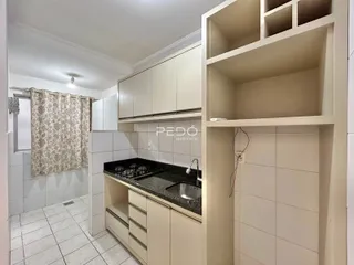 Vista interna de uma cozinha com armários e revestimento de azulejos brancos.