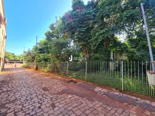Vista da entrada da propriedade com muro e vegetação ao lado de uma estrada de paralelepípedos.