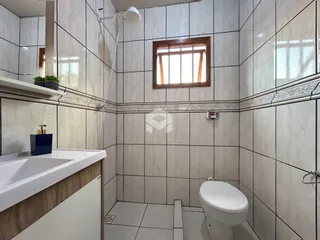 Foto de um banheiro com revestimento de azulejos brancos e uma janela.