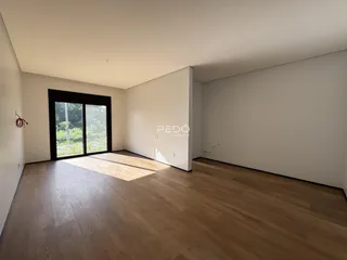 Interior de uma sala com piso de madeira clara e grande janela.
