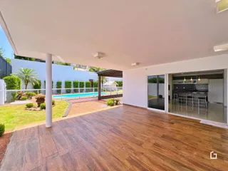Vista de uma área externa coberta com piso de madeira conectada a uma piscina e jardim.