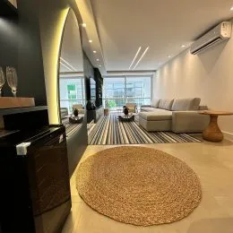 Sala de estar com sofá e piso claro e vista para o exterior.
