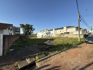 Vista externa de um terreno com vegetação e construções ao fundo.