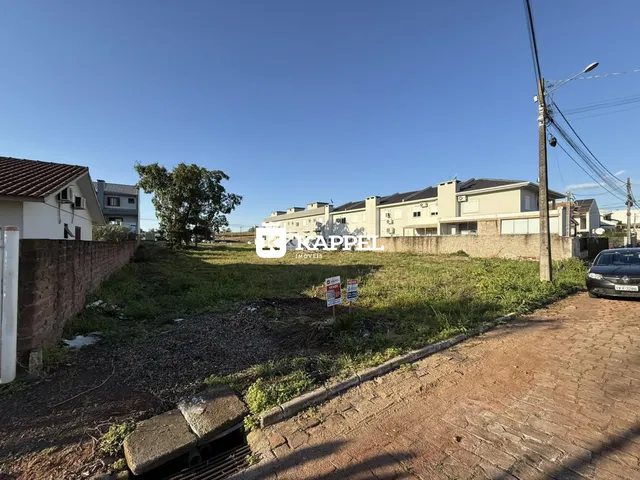 Vista externa de um terreno com vegetação e construções ao fundo.