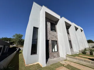 Fachada moderna de uma casa em Lajeado, Brasil, com revestimento branco e detalhes em tijolo aparente.