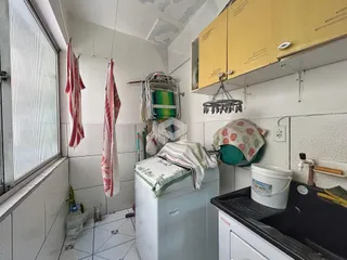 Foto interna de um espaço com máquina de lavar e roupas penduradas.